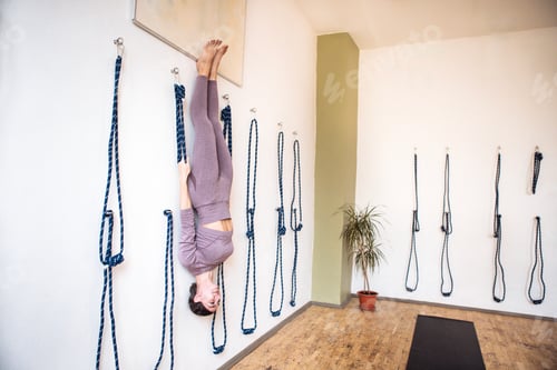 Preview: Female yoga practitioner performing an inversion pose while suspended from ropes