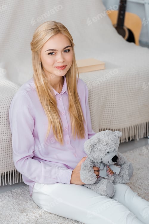 Preview: attractive woman sitting on carpet with teddy bear in hands