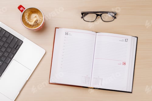 Preview: An open notepad with blank pages placed on a desk alongside a laptop and various office supplies