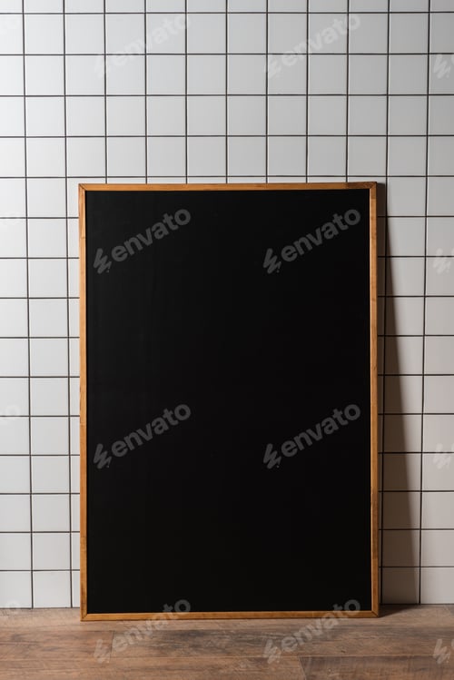 Preview: empty chalkboard in wooden frame standing at white tiled wall