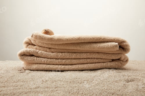 Preview: close up view of pile of towels with seashell on sand on grey backdrop