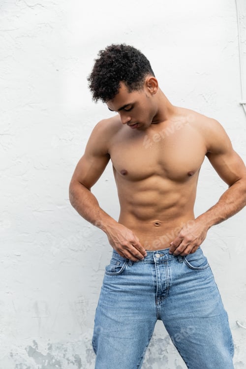 Preview: Muscular and strong young cuban man near white building on city street in Miami during summer