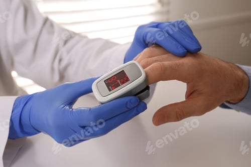 Preview: Doctor checking patient's oxygen level with pulse oximeter at light grey table, closeup