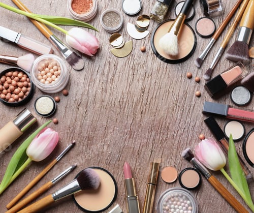 Preview: Many different makeup products and spring flowers on color background, flat lay. Space for text