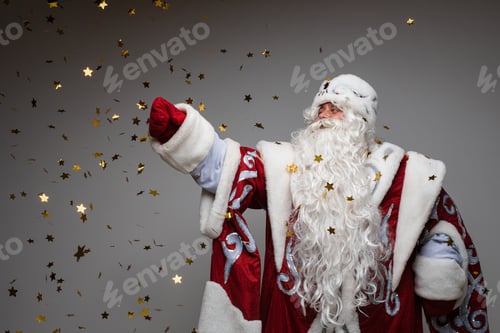 Preview: Playful Santa Claus catching golden stars shaped confetti on gray studio background