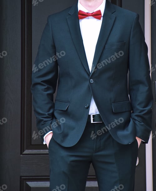 Preview: Handsome young man standing in front of door dressed in formal suit and red bow tie hands in pockets