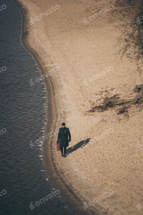 Preview: high angle view of man with luggage walking by sandy beach in autumn