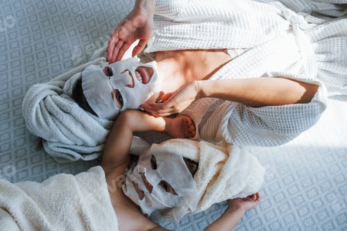 Preview: Mother and daughter have spa day with beauty masks on faces. Lying down on bed with towels on heads