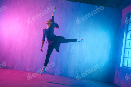 Preview: Modern dance girl dancer dancing in neon light doing gymnastic exercises in studio, copy space.