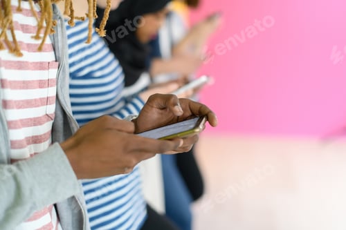 Preview: diverse teenagers use mobile devices while posing for a studio photo in front of a pink background