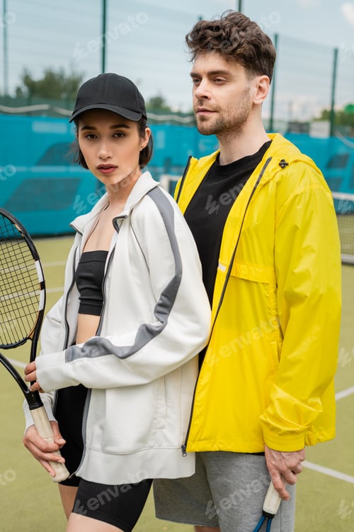 Preview: sport, fashionable man and woman standing on court with tennis racquet, sporty couple, hobby
