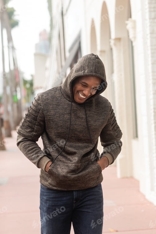 Preview: happy african american man in hoodie walking with hands in pockets in Miami