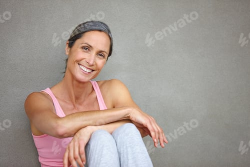 Preview: Portrait of an attractive mature woman in gymwear sitting against a gray wall