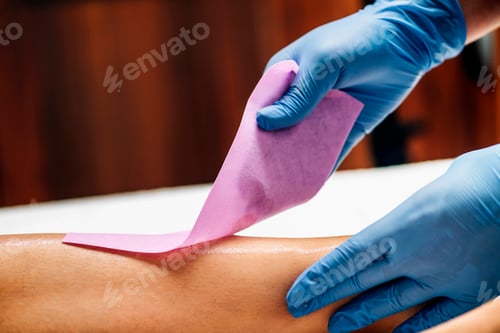 Preview: Waxing - Beautician Removing Unwanted Hair from Female Leg with Wax Strips