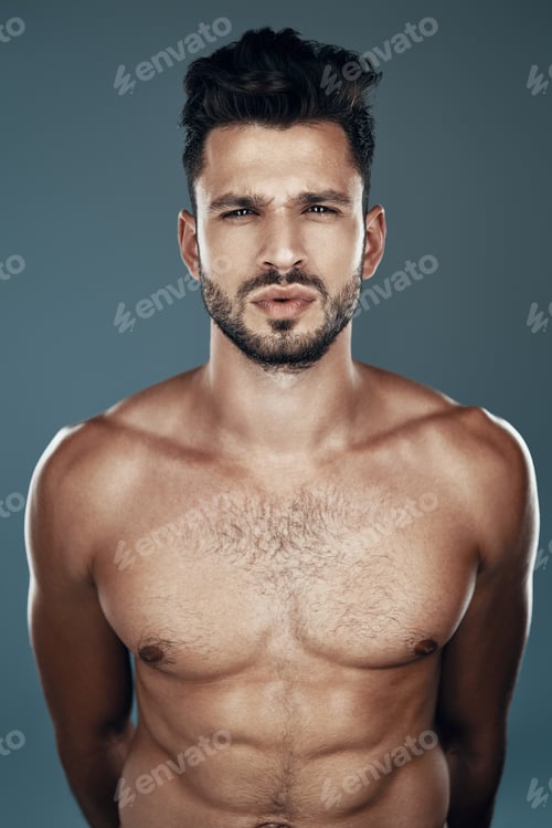 Preview: Handsome young shirtless man looking at camera while standing against grey background