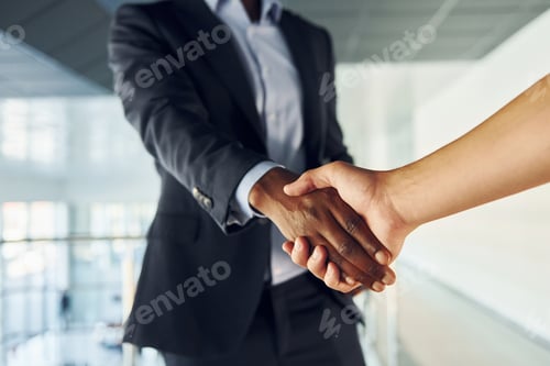 Preview: Doing handshake with customer. Young african american businessman in black suit is indoors