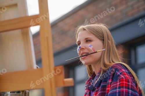 Preview: A young girl artist paints picture with a brush on a canvas that stands on an easel