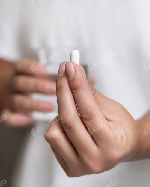 Preview: Woman in white t-shirt holding white pill in fingers and water glass in hand closeup