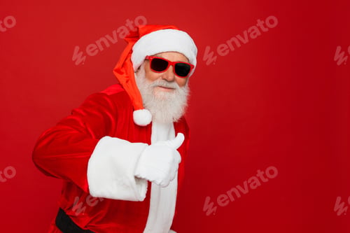 Preview: Santa Claus in sunglasses showing thumb up gesture empty space isolated on red color background.