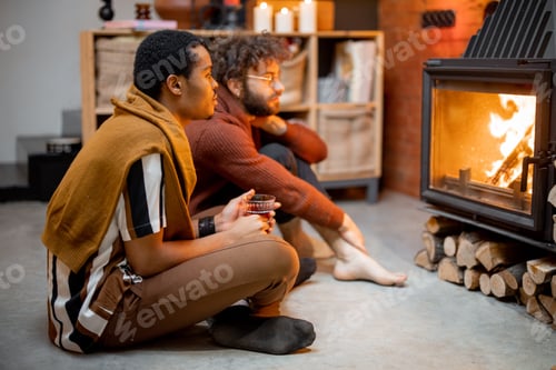 Preview: Two men sitting together by the burning fireplace at cozy home