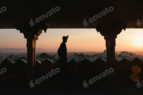 Preview: Silhouetted tourist looking out from City Palace at sunset, Lake
