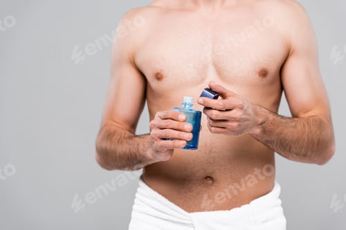 Preview: cropped view of muscular man holding bottle with after shave lotion isolated on grey