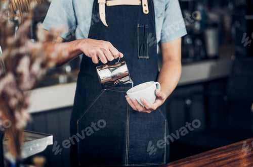 Preview: Man barista pour milk into hot coffee cup at counter bar