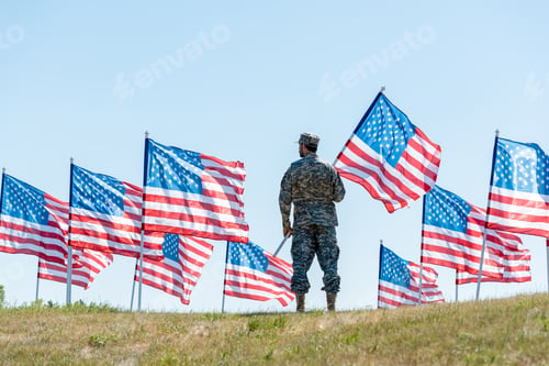 Preview: selective focus of soldier in military uniform and cap standing and holding american flag