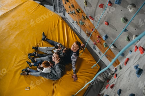 Preview: High angle shot of family with children sitting on a mat at gym with climbing walls in the