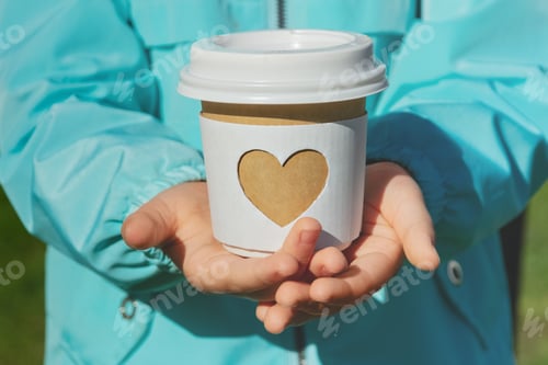 Vista previa: paper cup with carved white heart in children's arms of child in blue jacket