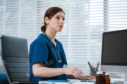 Preview: Doctor working with laptop computer and writing on paperwork.