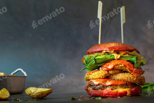 Preview: Closeup shot of a tall burger with onion rings and village potatoes on the side