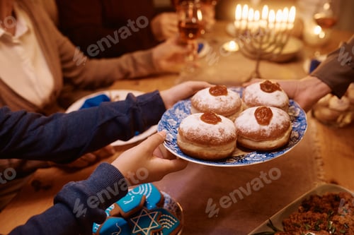 Preview: Close up of Jewish family having Hanukkah jam filled donuts for dessert at dining table.