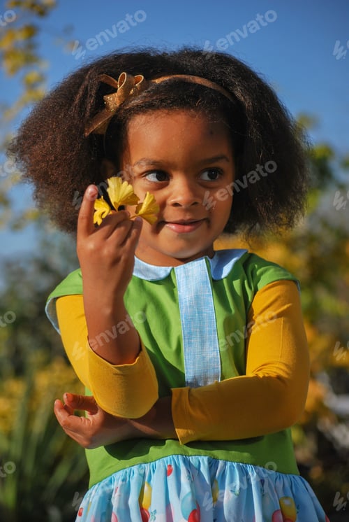Preview: Cute little girl of mixed race wearing a handmade dress, playing outside picking flowers in fall