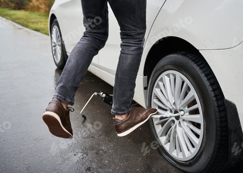 Preview: Young man repairing car wheel on the street.