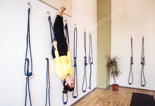 Preview: Woman practicing yoga in an inverted position, suspended by ropes on a wall