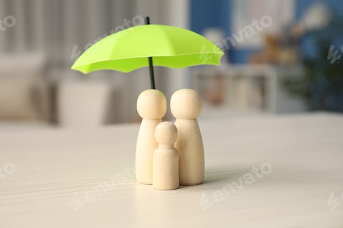 Preview: Human figures under umbrella on white wooden table indoors. Insurance concept