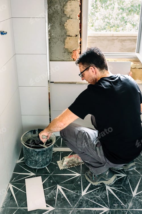 Preview: Mason taking cement from bucket to lay bathroom tiles