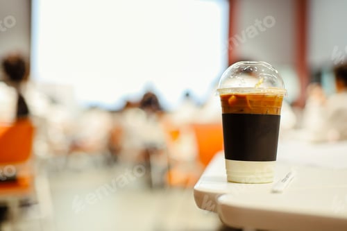 Preview: Close up glass of ice latte with blurred people in business workshop and presentation.Beverage at th
