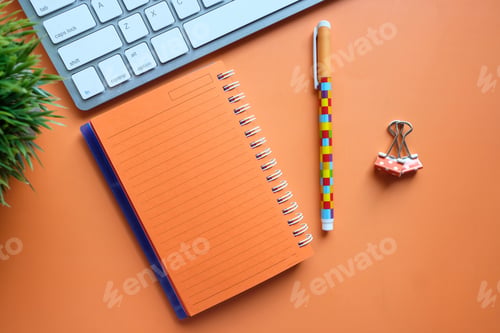 Preview: orange color notepad, keyboard, pen on desk
