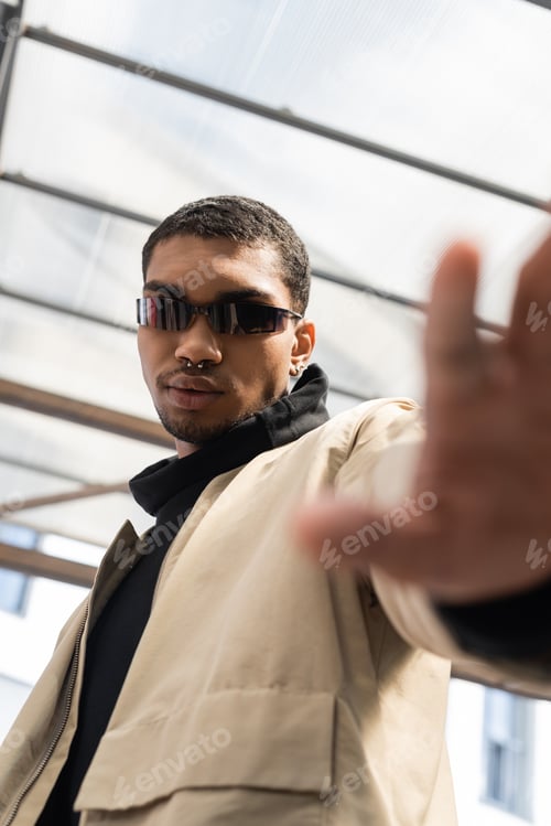 Preview: low angle view of young african american in stylish sunglasses standing with outstretched hand under