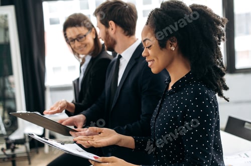 Preview: Side view to successful multiracial people, business partners, are standing in their modern office