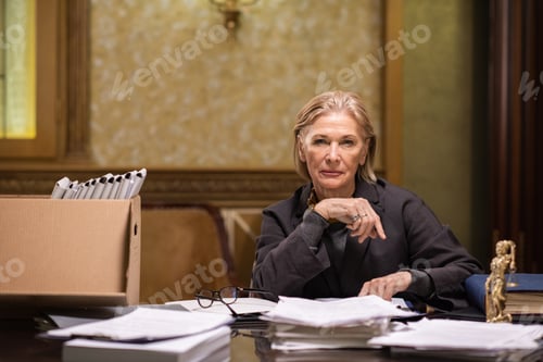 Preview: Confident mature female professional sitting by workplace