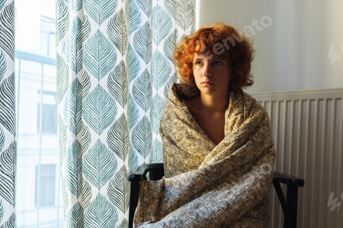 Preview: Sleepy teenage girl, in blanket, sitting on chair near radiator