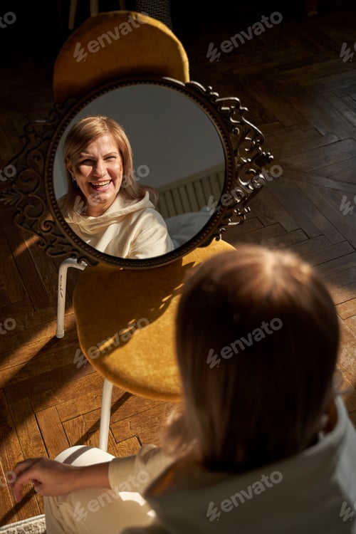 Preview: Caucasian mature female smiling in mirror reflection on wooden floor in cozy