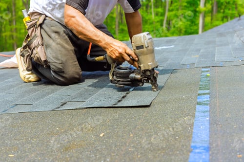 Preview: Roofer worker installing new bitumen shingles on a roof used an air pneumatic nail gun.