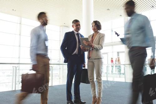 Preview: Front view of diverse business executives discussing over digital tablet in office lobby