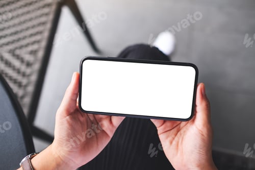 Preview: Top view mockup image of a woman holding mobile phone with blank white desktop screen