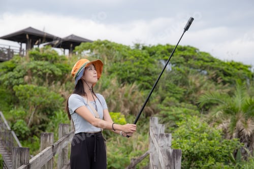 Preview: Woman walk along the hiking trail with hold with 360 camera to take photo and video at countryside