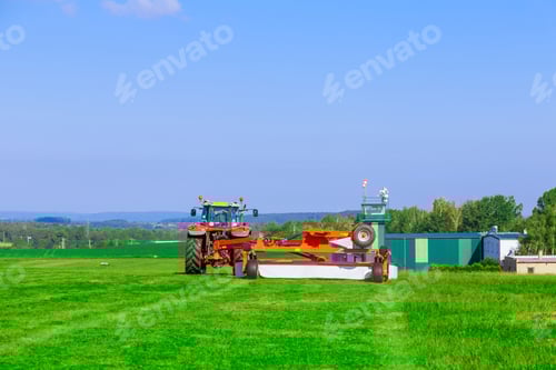 Preview: A large rotary mower mows the grass on the field near the building.